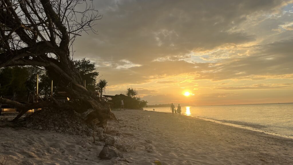 Golden sunset over the beach in the Gili Islands, Indonesia with people walking along the shoreline
