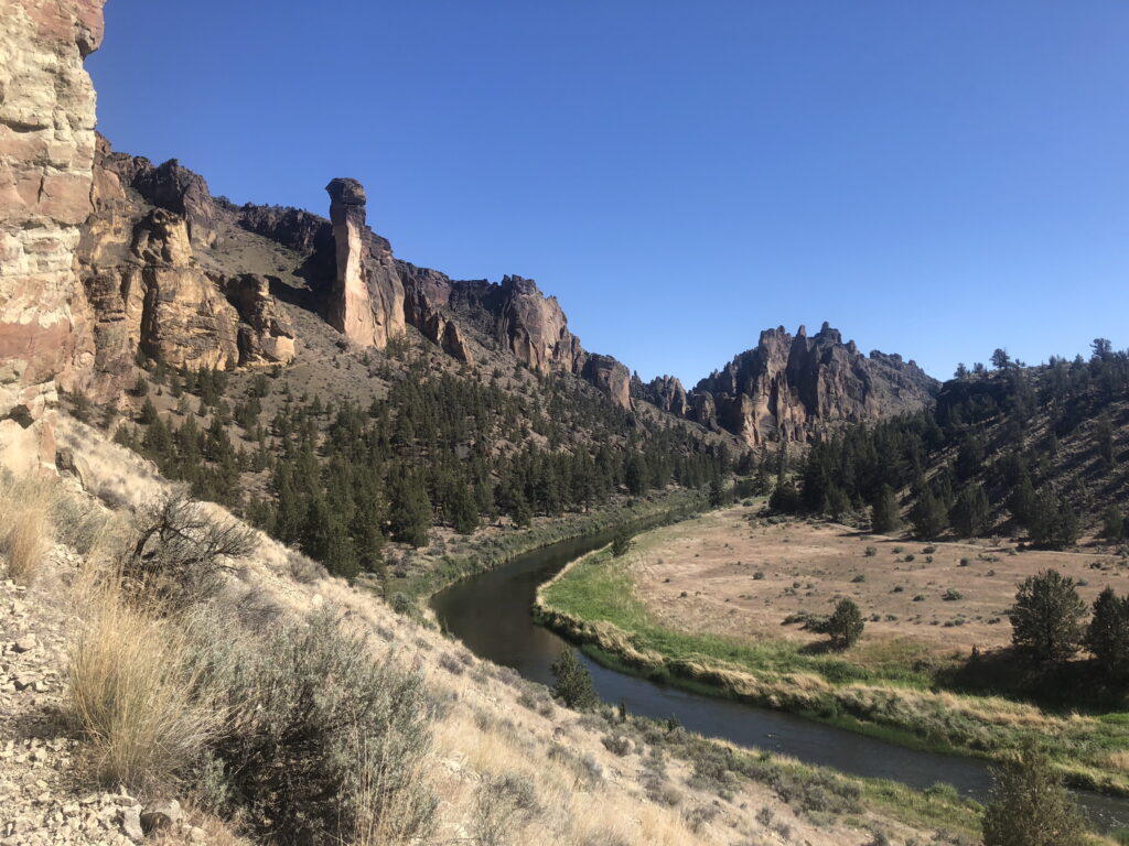 Smith Rock State Park in Central Oregon with the Crooked River and canyon cliffs under a clear blue sky.