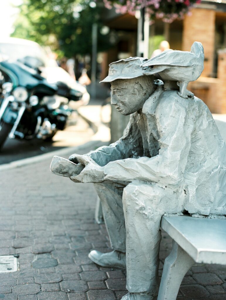 The Traveler statue in downtown Bend, Oregon, showing a seated man looking into his hands with birds perched on his shoulders.